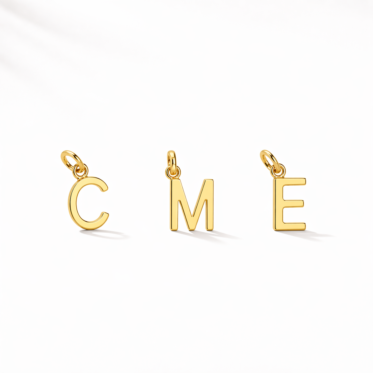 Three gold letter pendants spelling 'COME' on a white background