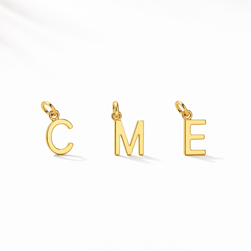 Three gold letter pendants spelling 'COME' on a white background