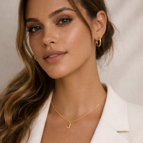 Woman wearing gold hoop earrings and a gold necklace with a 'J' pendant against a neutral background