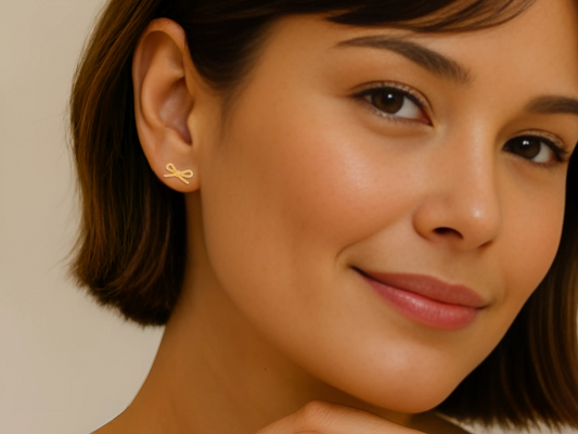 Close-up of a woman wearing gold bow shaped earrings with a neutral background