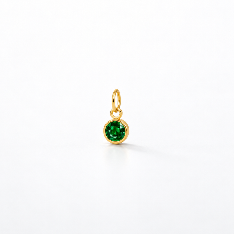 A small gold charm pendant featuring a round, faceted green gemstone in a bezel setting, suspended from a gold loop, shown on a clean white background.